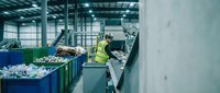 Industrial waste sorting facility with worker in safety gear operating recycling equipment for environmental sustainability and circular economy processes.