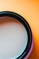 Close-up view of camera lens filter rim against vibrant orange background showing circular shape and metallic details, creating minimalist abstract photography composition.