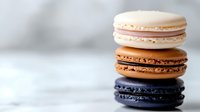 Stack of colorful French macarons with white, caramel and black flavors on marble surface for bakery menu, dessert photography and culinary branding.