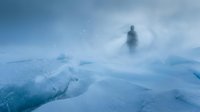 Solitary figure standing in heavy snowstorm amid frozen landscape with snow-covered terrain and blizzard conditions, conveying isolation and winter adventure.