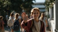 Cheerful Caucasian teenage boy with curly hair waving hello on school campus, wearing burgundy cardigan and backpack, with blurred students in background.