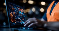 African American male professional analyzing digital network visualization on laptop screen in dark office, glowing orange and blue data connections display.