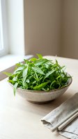 Fresh arugula microgreens with water droplets in concrete bowl on wooden table near window, ready for culinary use and food styling.