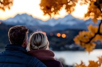 Romantic couple watching sunset over mountain lake, framed by golden autumn leaves. Cozy fall evening with bokeh lights and warm atmosphere creates intimate moment.