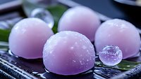 Traditional Japanese mochi dessert in soft purple color with delicate sugar coating served on bamboo plate with green leaf garnish, macro food photography.