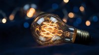 Vintage incandescent bulb with glowing filament against dark background with bokeh lights, suitable for energy, innovation, and creativity concepts.