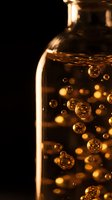 Glass bottle filled with golden bubbles and liquid against dark background, suitable for cosmetics, skincare, perfume, and luxury product packaging design.