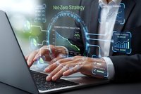 Professional businessman working on laptop with holographic net-zero strategy interface displaying carbon footprint reduction metrics and sustainability data.