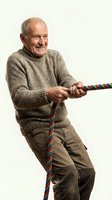 Happy senior Caucasian man in sweater pulling colorful rope in tug of war game isolated on white background for teamwork and competition concepts.