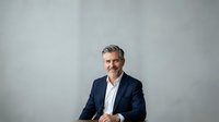Middle-aged Caucasian male professional in dark blazer and white shirt against neutral gray background, suitable for corporate portraits, business websites, and executive headshots.