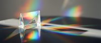 Transparent crystal prism refracting light into vibrant rainbow spectrum on neutral surface, creating colorful light patterns for science and educational design projects.