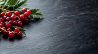 Fresh red currants with green leaves on dark slate background, selective focus with copy space for food photography and menu design.