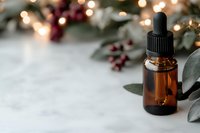 Essential oil amber glass dropper bottle with eucalyptus leaves and red berries on marble surface, soft bokeh lights creating festive holiday atmosphere.