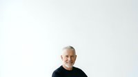 Mature man with gray hair and light skin tone wearing black casual shirt, smiling at camera against white background for portrait and professional use.