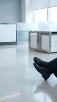 Person lying on modern office floor wearing black leather dress shoes, suggesting workplace accident, burnout, or business stress concept.