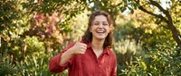 Young woman with curly hair giving thumbs up gesture in autumn park setting with golden foliage background for positive lifestyle and success concepts.