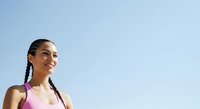 Young woman with dark braided hair and medium brown skin tone wearing pink athletic tank top against clear blue sky, suitable for fitness, wellness, and sports marketing.