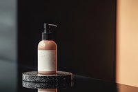 Minimalist cosmetic bottle with pump dispenser on black stone pedestal against warm gradient background, modern luxury skincare packaging mockup.