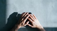 Young Caucasian man covering face with hands showing stress, depression, anxiety, mental health struggles against concrete wall background.