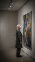 Senior woman with gray hair admiring abstract painting in modern art gallery, contemplating colorful artwork in contemporary museum space.