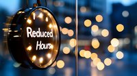 Round illuminated sign with reduced hours text against blurred bokeh lights background, creating moody business atmosphere during special operation period.