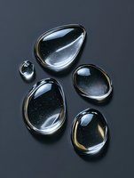 Clear water drops on dark background with reflective surfaces and golden highlights creating elegant organic shapes for luxury cosmetic advertising.
