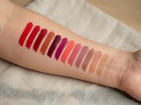 Colorful lipstick swatches on woman's arm showing various shades from red to pink to nude tones for cosmetic testing and makeup selection.