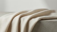 Soft beige wool blanket draped over concrete surface creating elegant minimalist composition for home decor and textile design projects.