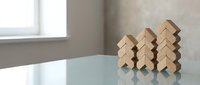 Wooden building blocks arranged in ascending stacks on glass table surface creating growth pattern in modern minimalist interior setting.
