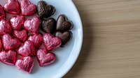 Heart-shaped chocolate candies in red and brown foil wrappers arranged on white plate, romantic Valentine's Day sweets for love celebration.