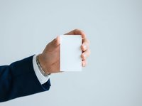 Male professional in dark business suit holding blank white card against neutral background for corporate branding and marketing presentations.