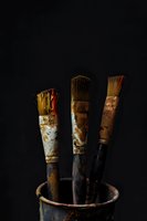 Old worn artist paintbrushes with natural bristles in rustic metal holder against dark background, dramatic moody lighting creates artistic atmosphere.