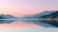 Serene mountain lake at dawn with pink purple sky reflecting in calm water surrounded by layered hills creating peaceful landscape for meditation and wellness content.