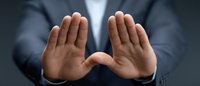 Male hands in business suit showing stop gesture against dark background, demonstrating rejection, denial or protection. Professional corporate concept.