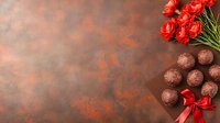 Dark chocolate truffles with red satin bow and fresh roses on rustic brown textured background with copy space for Valentine's day or romantic occasion.