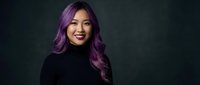 Young Asian woman with vibrant purple hair smiling confidently in black turtleneck against dark background for professional headshot and portrait photography.