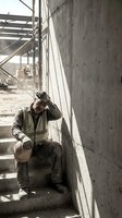 Exhausted construction worker sitting on concrete stairs at building site holding hard hat and head in hands showing fatigue and stress.