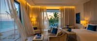 Luxury beachfront hotel room with ocean view, golden ambient lighting, modern furnishings, and floor-to-ceiling windows overlooking tropical paradise for hospitality and travel design.