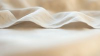 Soft cream linen fabric with delicate folds and waves, showcasing natural texture and elegant draping for textile, fashion, and interior design projects.