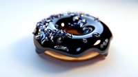 Dark chocolate glazed donut with black sprinkles on white surface, close-up view showing glossy texture and rich details. Sweet dessert photography.