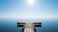 Wooden dock extending into calm blue water under clear sky, serene lakeside or seaside landscape for travel, wellness, and meditation design projects.