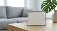 Blank photo frame on wooden coffee table in modern living room with gray sofa and monstera plant, mockup for design presentation.
