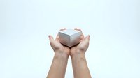 Hands holding small white gift box with pink ribbon on clean background for product presentation and marketing materials.