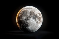 Detailed view of lunar surface showing craters and textures with dramatic side lighting creating golden glow effect against dark space background.