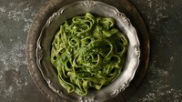 Fresh green spinach pasta fettuccine served on vintage silver plate against dark rustic background, top view. Homemade Italian cuisine for restaurant menu.