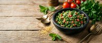Fresh tabbouleh salad with parsley, tomatoes and bulgur wheat in black bowl on rustic wooden table with herbs and ingredients for healthy Mediterranean cuisine.