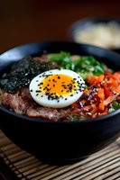 Korean bibimbap bowl with marinated beef, soft-boiled egg topped with black sesame seeds, carrots, seaweed, and fresh herbs served in traditional black bowl.