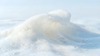 Frozen wave formation with crystalline ice structure and snow accumulation creating natural winter sculpture against pale sky backdrop for seasonal design projects.