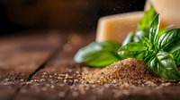 Fresh basil leaves next to scattered ground black peppercorns and coarse spices on rustic wooden surface with soft lighting and shallow depth of field.