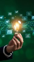 Businessman hand holding glowing light bulb with renewable energy icons and digital circuit connections on green background for sustainable innovation.
